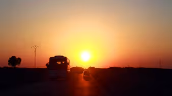 Vehicles drive down a road near the Tunisia-Libya border with the sun in the background