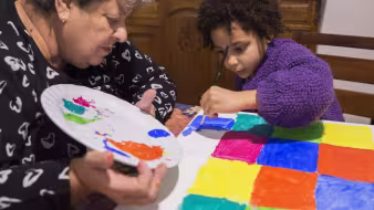 A grandmother and young grandchild painting at home