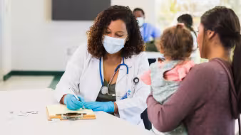 A woman holding a young child talks to a female pediatrician at a free clinic