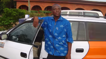 A man stands next to a taxi he got with the help of IOM's AVRR program