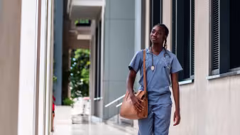A Black female nurse in blue scrubs walking outside