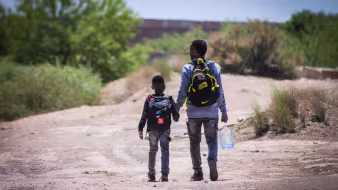 Father and son walk in front of the wall that divides Mexico from the United States