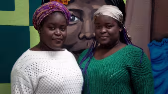 Two Haitian women stand in front of a mural in Mexico