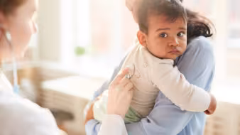 Mother holds her young child while doctor examines him with a stethoscope