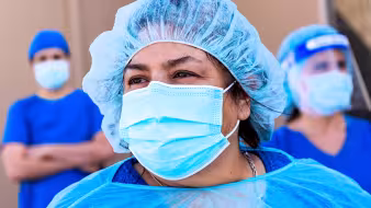 Three health-care workers wearing blue protective masks and gowns