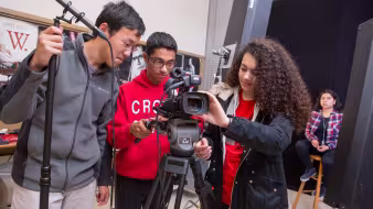 Three students in a digital filmmaking class set up a camera
