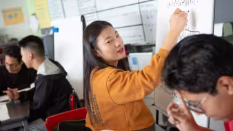 A high school student answers a math problem on a whiteboard
