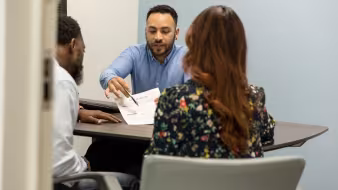 Three people sit at a desk and discuss a form