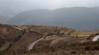 A road cuts across mountains and hills, with clouds in the background, in Huehuetenango, Guatemala