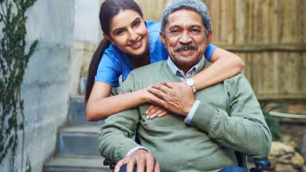  A young nurse hugs an elderly patient in a wheelchair