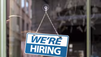 A blue "we're hiring" sign on a window