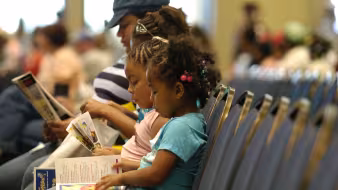 A woman and three children sit on a bench reading.