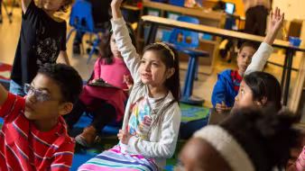 A third grader raises her hand in class