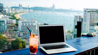 A laptop and cocktail on a ledge overlooking the beach