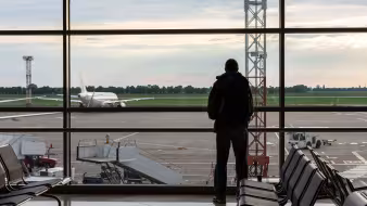 A man with a backpack stands in an airport and looks at a plane