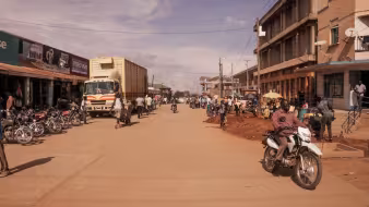 Motorcyclists and pedestrians travel a road between buildings in Arua, Uganda