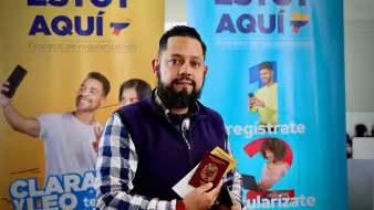 A Venezuelan man holds a passport in front of a sign for Ecuador's regularization process