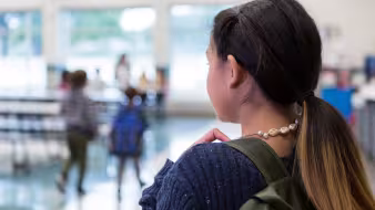 A middle school girl standing alone in a school cafeteria