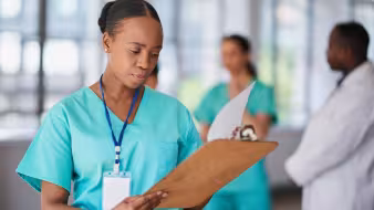 A woman wearing scrubs in a health-care setting reviews a chart