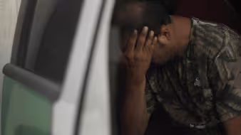An apprehended migrant sits in a truck with his hands in his face