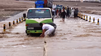 People pulling vehicles from a flooded road in an Afghan village