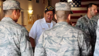 Two men in military attire stand with a veteran