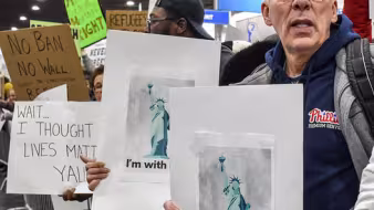A man holds a sign protesting the travel ban at an airport