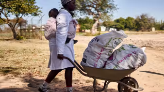 A woman in Zimbabwe pushes a wheelbarrow.