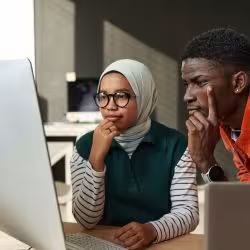 Two young IT engineers look at a computerscreen. (Photo: iStock.com/mediaphotos)